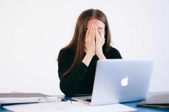 Woman stressed, holding her face in her hands while sitting in front of computer.