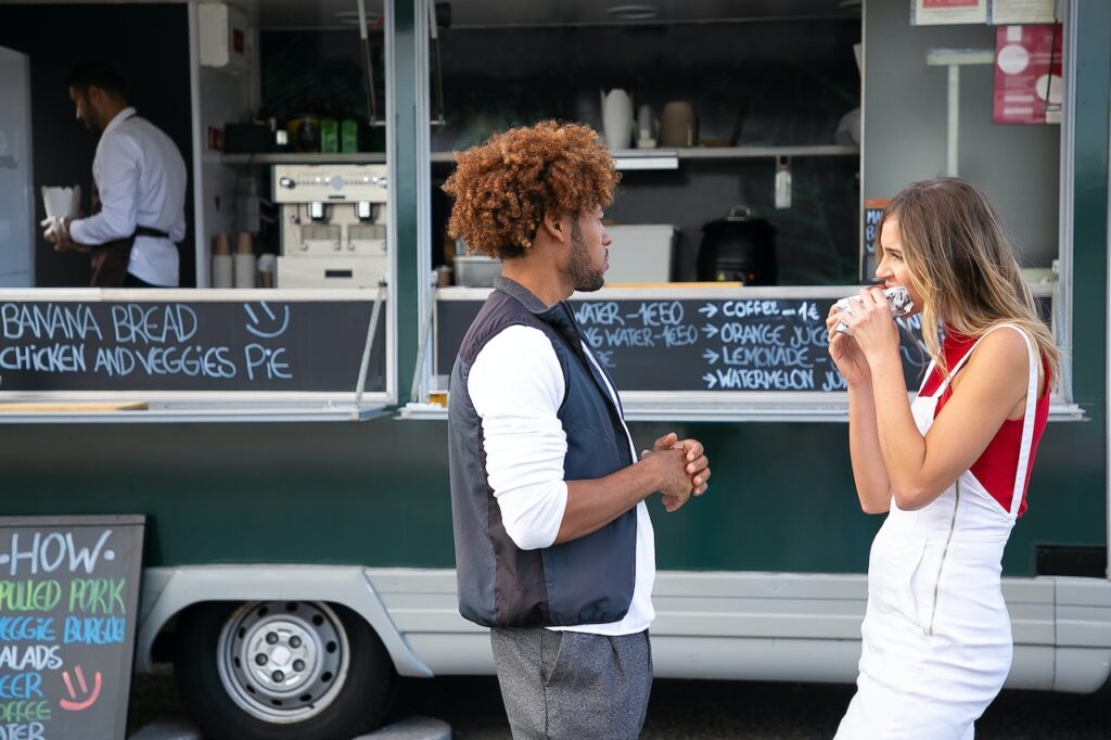 Black man and blonde girl eating at a food truck.