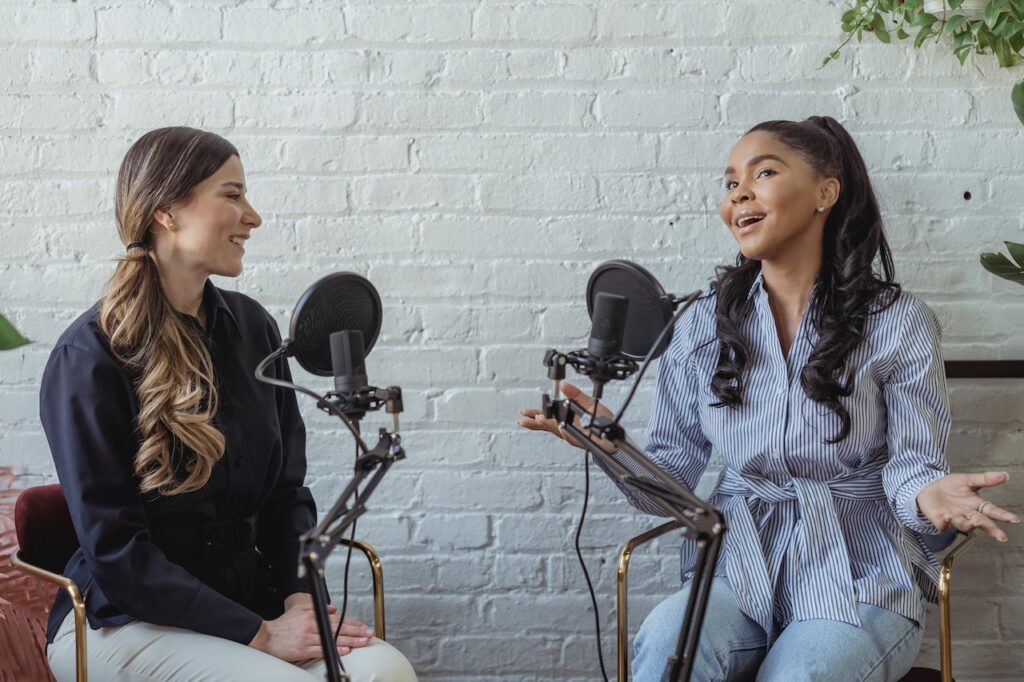 Two women talking into microphones for a radio or podcast show.