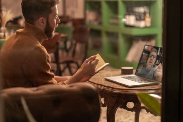 Young man having virtual meeting while reading notes in cozy cafe