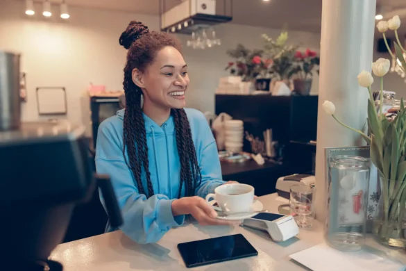 Mixed-race young beautiful female barista handing cup of coffee to customer. Bartender work.